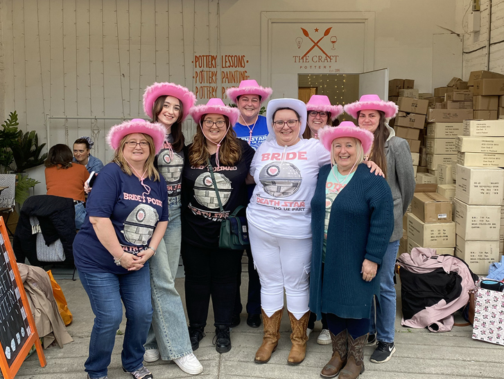 Hen party group outside The Craft Pottery wearing pink fluffy cowboy hats and Bride wearing white fluffy cowboy hat